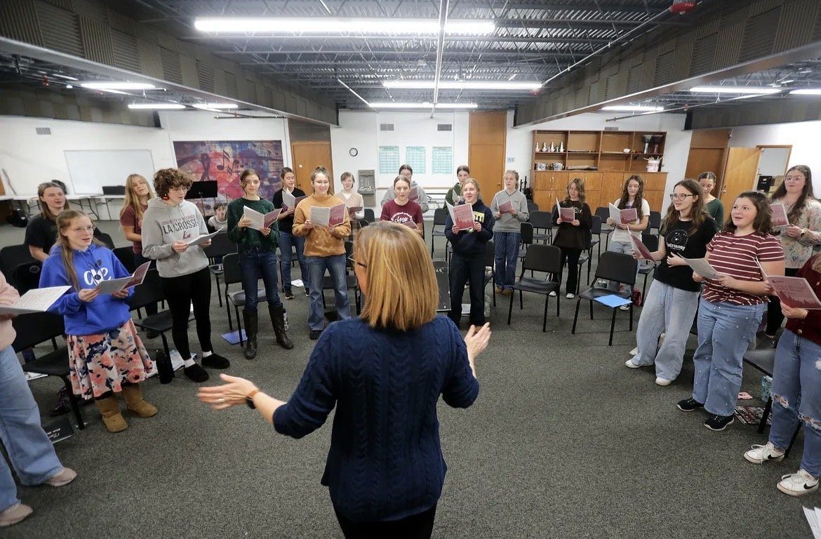 Cathy leading a choir rehearsal, singers standing in a wide circle