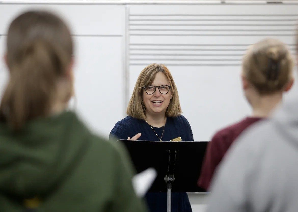 Cathy smiling at a music stand, working with singers in rehearsal